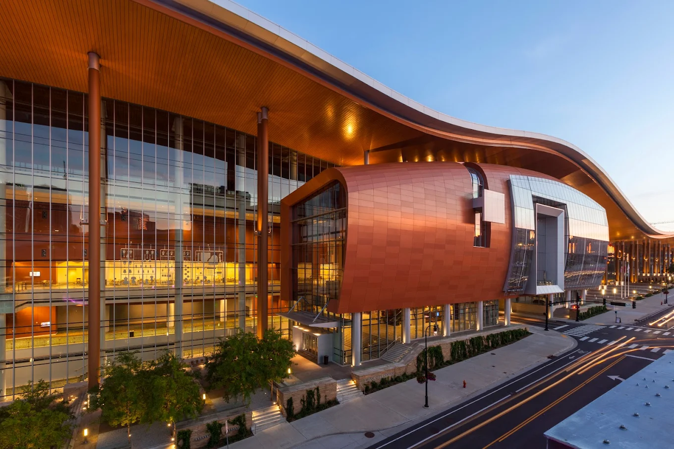 Music City Center at dusk, its copper roof curving over a lit glass facade in downtown Nashville