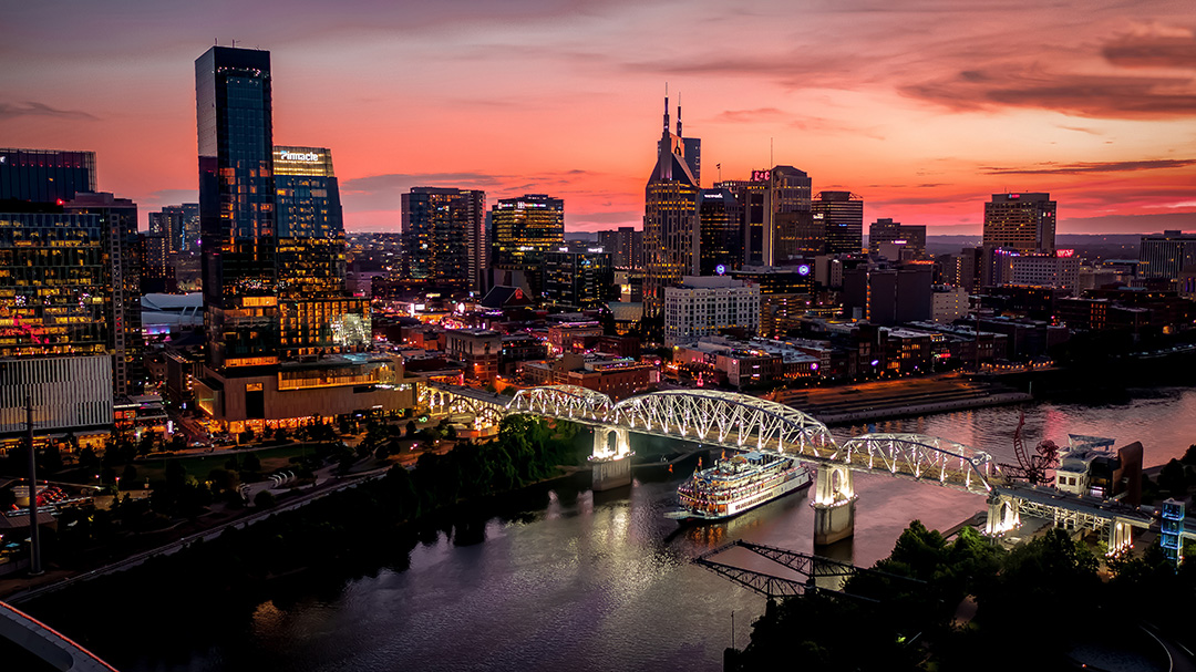 The Nashville skyline lit at dusk, with the Cumberland River and a bridge in the foreground