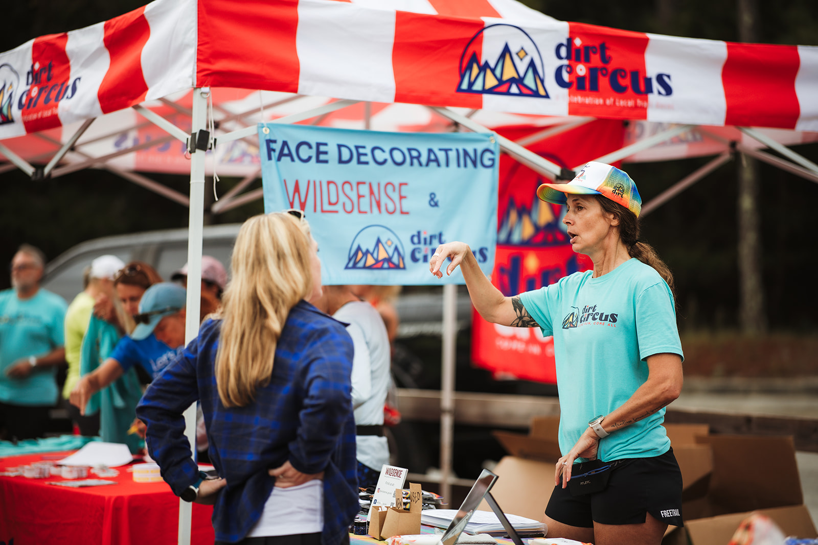 A person in a Dirt Circus shirt talking with visitors across a table under a red and white striped tent