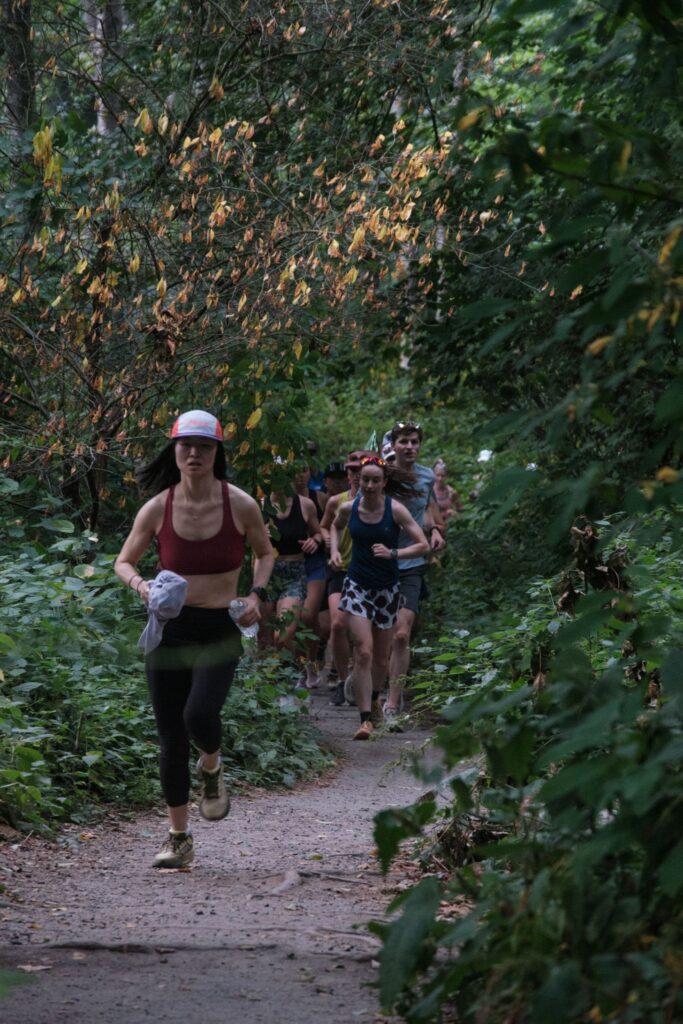 Runners on a narrow forest trail under a closed green canopy